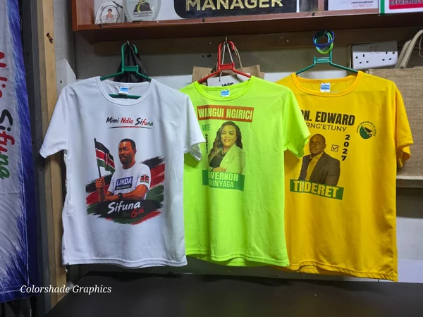 Three printed campaign t-shirts on hangers in white, lime green and yellow, each carrying a full-colour candidate design