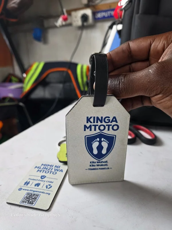 Branded Kinga Mtoto luggage tag with a QR code, held beside a matching bookmark tag